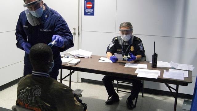 U.S. Coast Guard Health Technician Nathan Wallenmeyer (L) and Customs Border Protection (CBP) Supervisor Sam Ko conduct prescreening measures on a passenger arriving from Sierra Leone at O'Hare International Airport's Terminal 5 in Chicago 