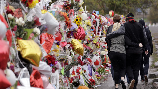 People walk arm-in-arm past a memorial for victims outside Marysville-Pilchuck High School following a deadly shooting there nearly a week earlier Oct. 30, 2014, in Marysville, Wash. 