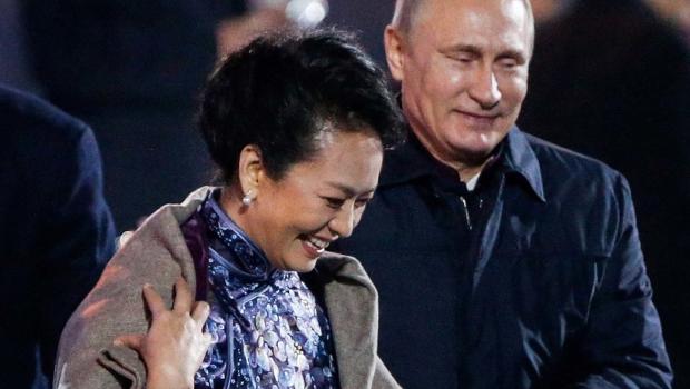 Russia's President Vladimir Putin helps put a shawl on Peng Liyuan, wife of China's President Xi Jinping 