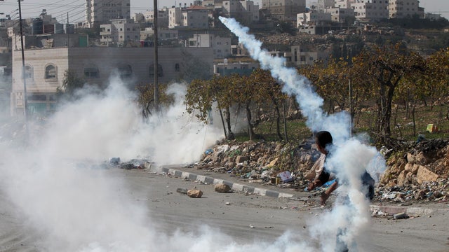 Palestinian throws back a tear gas grenade at Israeli soldiers during clashes on the outscirts of the West Bank city of Hebron on Nov 11, 2014.  