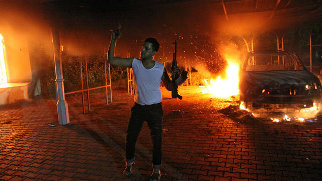 An armed man waves his rifle as buildings and cars are engulfed in flames after being set on fire inside the U.S. compound in Benghazi Sept. 11, 2012. 