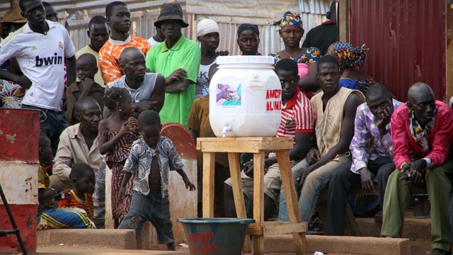 Malians sit near a container to wash hands in the village of Kouremale near the border with Guinea 