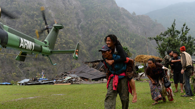 A Nepalese resident injured in an earthquake is carried by a relative towards an Indian Army helicopter as others follow at Lapu, in Gorkha 