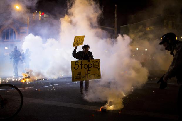 Protester holds sign as clouds of smoke and crowd control agents rise, shortly after citywide curfew went into effect in Baltimore on Tuesday night, April 28, 2015 