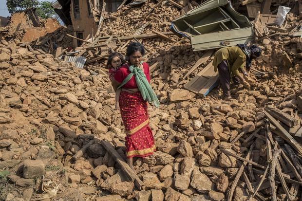 A woman carries a child through the rubble of buildings which collapsed during an earthquake in Sathighar, north of Kathmandu 
