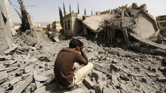 A guard sits on the rubble of the house of Brigadier Fouad al-Emad, an army commander loyal to the Houthis 