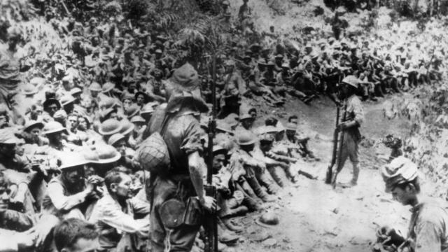 Japanese soldiers stand guard over American war prisoners just before the start of the Bataan Death March following the Japanese occupation of the Philippines.  