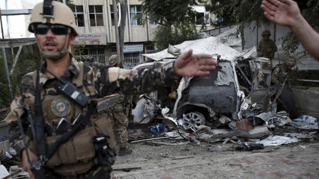 Members of the Afghan security forces keep watch in front of a damaged car that belongs to foreigners after a bomb blast in Kabul, Afghanistan, Aug. 22, 2015. 