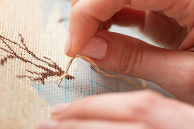 Woman hands doing cross-stitch. A close up of embroidery. 