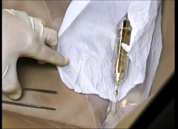 In this Feb. 19, 2015 image made from video provided by the Moldova General Police Inspectorate, an investigator looks at a vial containing cesium-135 on the driver's seat of Valentin Grossu's car following his arrest in Chisinau 