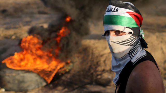 A masked Palestinian protester passes by burning tires during clashes with Israeli troops near the border between Israel and central Gaza Strip Oct. 14, 2015. 