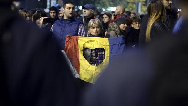 A woman holds a flag in front of a police line as thousands of people rally demanding government resignations as the death toll from a night club fire at the weekend reached 32, with dozens more in the hospital in critical conditions, in Bucharest, Romani 