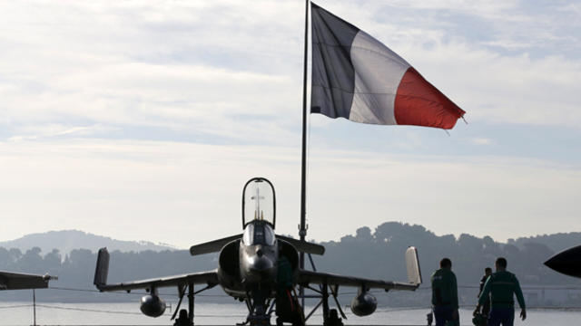 Flight deck crew work around a Super Etendard fighter jet as a French flag flies aboard the French nuclear-powered aircraft carrier Charles de Gaulle before its departure from the naval base of Toulon, France, Nov. 18, 2015. The carrier was being deployed 