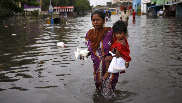A woman carries her child and milk packets as she wades through a flooded street in Chennai, India, Dec. 5, 2015. 