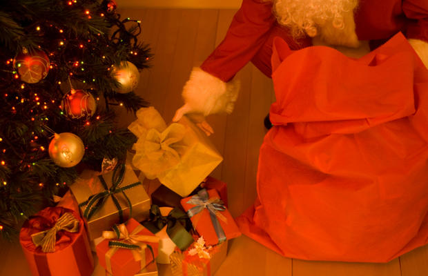 Santa Claus placing gifts under a Christmas tree 