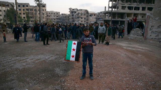 A boy carries an opposition flag as rebel fighters and civilians gather during the arrival of an aid convoy by the Syrian Arab Red Crescent and the United Nations to the rebel-held besieged town of Kafr Batna on the outskirts of Damascus, Syria, Feb. 23,  