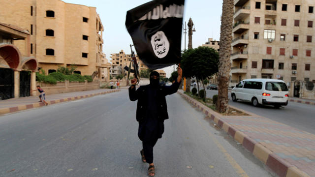 ​A member loyal to the Islamic State of Iraq and Syria waves a flag in Raqqa, Syria, June 29, 2014. 