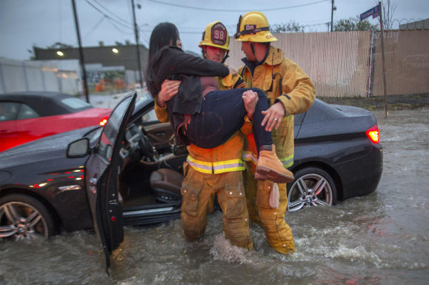 A firefighter carries a woman from her car after it was caught in street flooding as a powerful storm moves across Southern California on Feb. 17, 2017, in Sun Valley, California. 