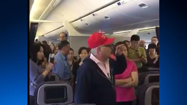 A United Airlines passenger wearing a red "Make America Great Again" cap gestures with his hand on a New Jersey-bound flight from Shanghai on May 21, 2017. 