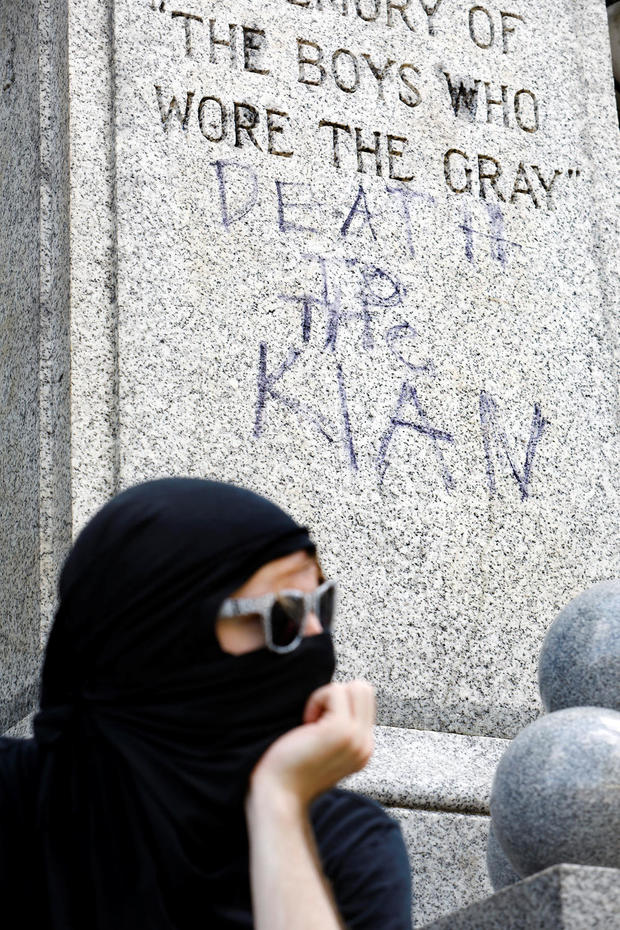 A masked counter-protester rests in front of the base of a Confederate statue scrawled with the slogan "Death to the Klan" as demonstrators gather after a report of a rally by white nationalists was disseminated over social media in Durham 