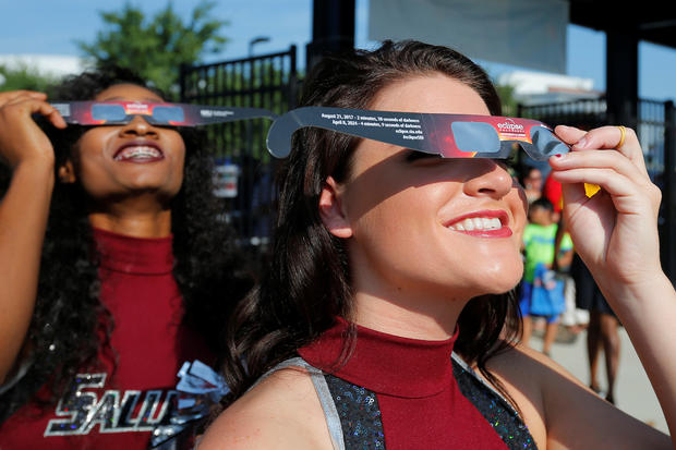 Cheerleaders use solar viewing glasses before welcoming guests to the football stadium to watch the total solar eclipse at Southern Illinois University in Carbondale 