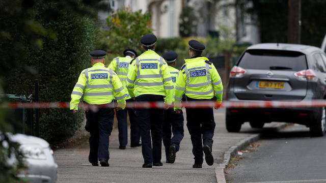 Police officers walk behind cordon tape set up around a property being searched after a man was arrested in connection with an explosion on a London Underground train, in Sunbury-on-Thames 