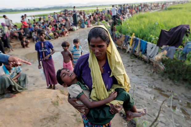A Rohingya refugee woman who crossed the border from Myanmar a day before, carries her daughter and searches for help as they wait to receive permission from the Bangladeshi army to continue their way to the refugee camps, in Palang Khali 