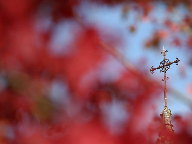 Autumn colored leaves frame the metal cross on the steeple of a church in Orvault 