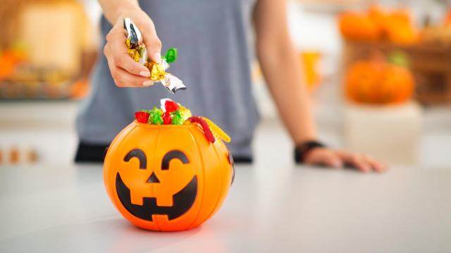 Woman putting trick or treat candy in halloween bucket 