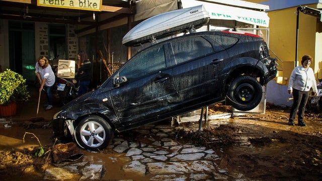 Staff at a car rental store clean up damage in front of a washed up vehicle following a powerful storm on the Greek island of Symi Nov. 14, 2017. 