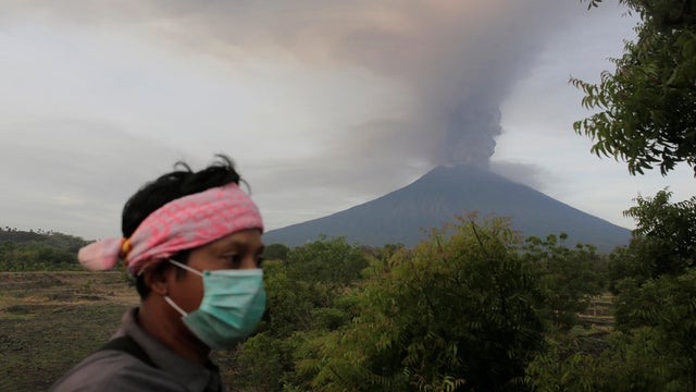 A villager walks as Mount Agung volcano erupts in the background in Kubu 