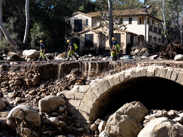 Montecito firefighters walk on a road damaged by mudslides in Montecito, California 