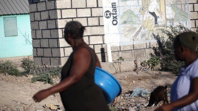 People walk past an Oxfam sign in Corail, a camp for people displaced after 2010 earthquake, on the outskirts of Port-au-Prince 