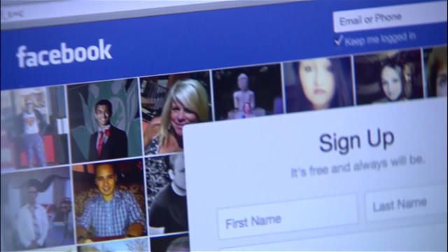 FILE PHOTO: A man is silhouetted against a video screen with a Facebook logo as he poses with a smartphone in this photo illustration 