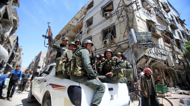 Members of the Syrian police hold their weapons as they sit on a back of a truck at the city of Douma, Damascus 