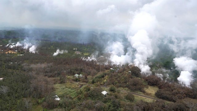 Aerial image of molten rock flowing and bursting to the surface threatening homes in a rural area in Hawaii 