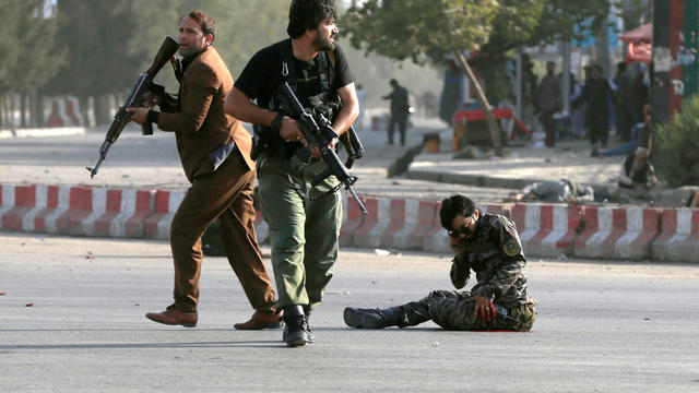 Members of Afghan security forces arrive as an injured man sits on the ground at the site of a blast in Kabul 