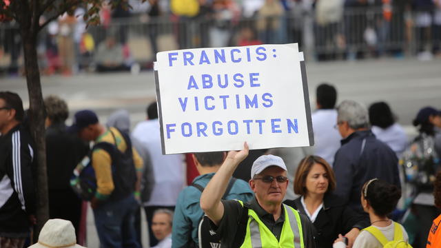 Activist with sign denouncing the church's alleged lack of 