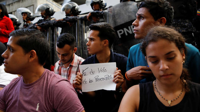 A mourner of the municipal lawmaker Fernando Alban holds a placard that reads, "Proof of life of all political prisoners" in front of riot police members standing outside the headquarters of Bolivarian National Intelligence Service (SEBIN) in Caracas 