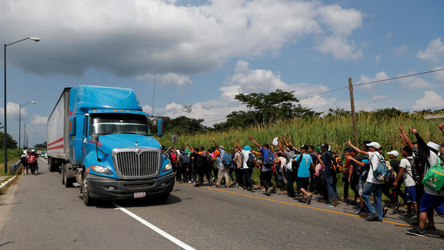 Migrants, part of a caravan traveling from Central America en route to the United States, wave to a truck while walking by the road that links Ciudad Hidalgo with Tapachula 