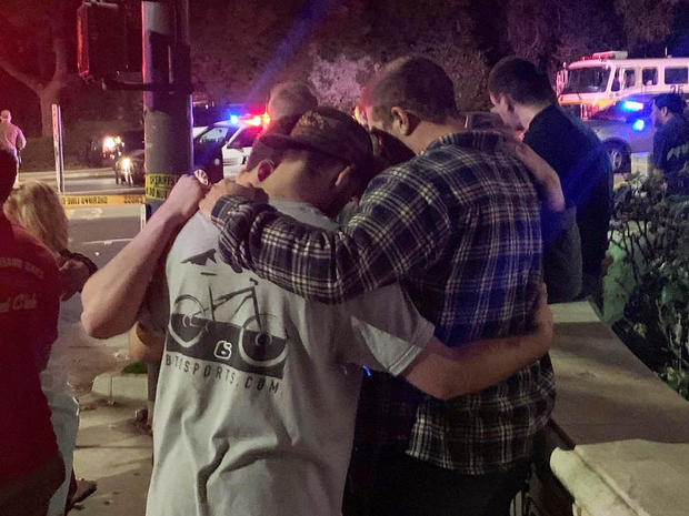 People stand behind cordon tape and hold each other, after the shooting in Thousand Oaks, California 