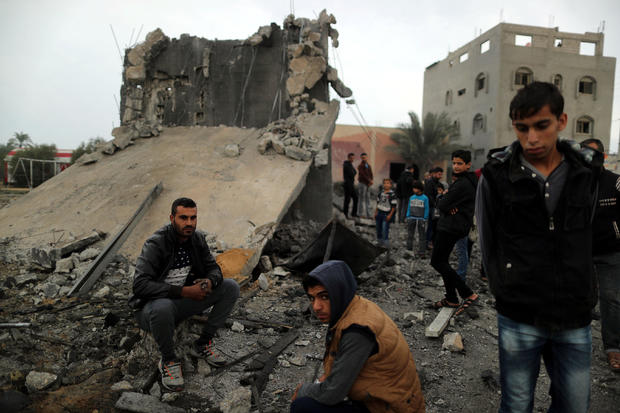 Palestinians sit at the remains of a building that was destroyed by an Israeli air strike, in Khan Younis in the southern Gaza Strip 