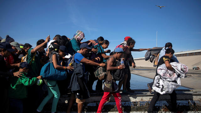 Migrants, part of a caravan of thousands traveling from Central America en route to the United States,cross the Tijuana river to reach the border wall between the U.S. and Mexico in Tijuana 