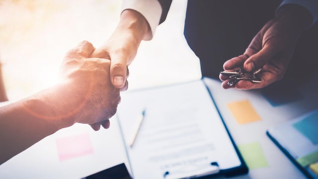 Agents are giving house keys of customer with handshaking after good deal at agency office. Real Estate and Agreement concept. 