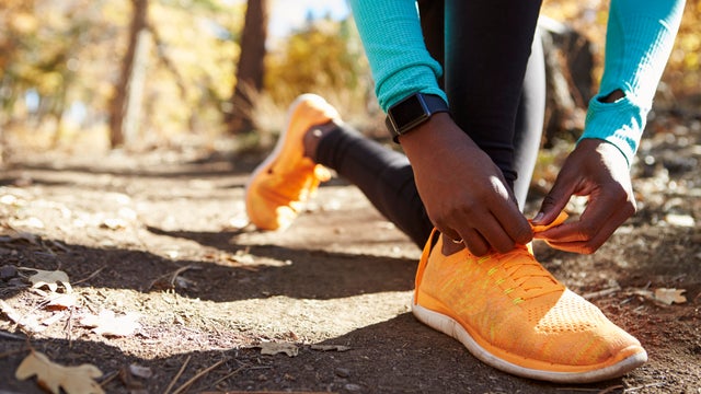 Black female runner in forest tying shoe, low section detail 