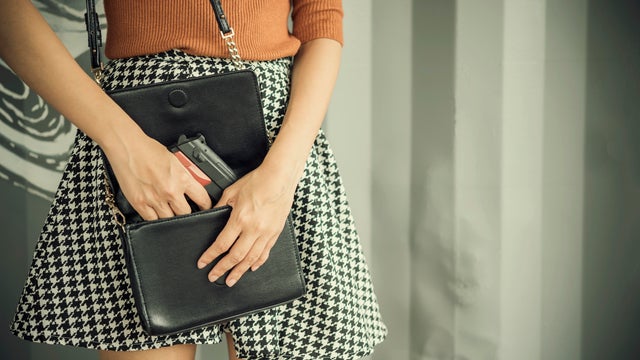 Photo of hand of young woman pulling a pistol out of her handbag with free copy space. Self defences concept 