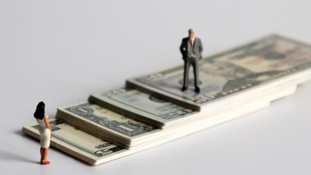 A miniature man and a miniature woman standing on a pile of bills. 