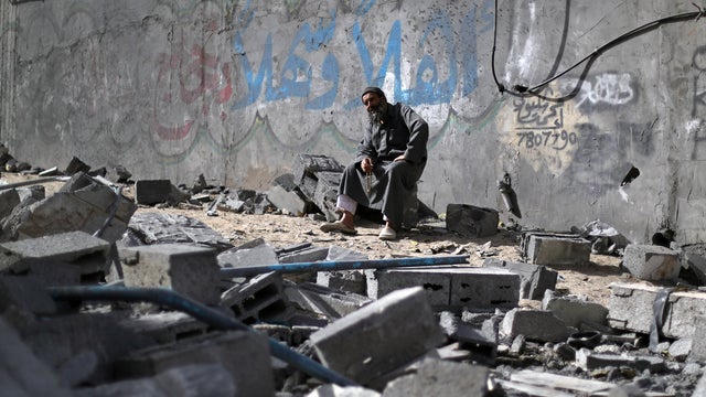 Palestinian man sits on debris near a building that was destroyed by Israeli air strikes, in Gaza City 
