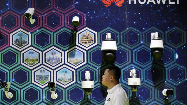 Man walks past surveillance cameras displayed at a Huawei booth at an exhibition during the World Intelligence Congress in Tianjin 