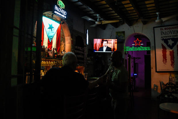 People watch a television broadcast of Puerto Rico's governor Ricardo Rossello's speech at a bar in San Juan 